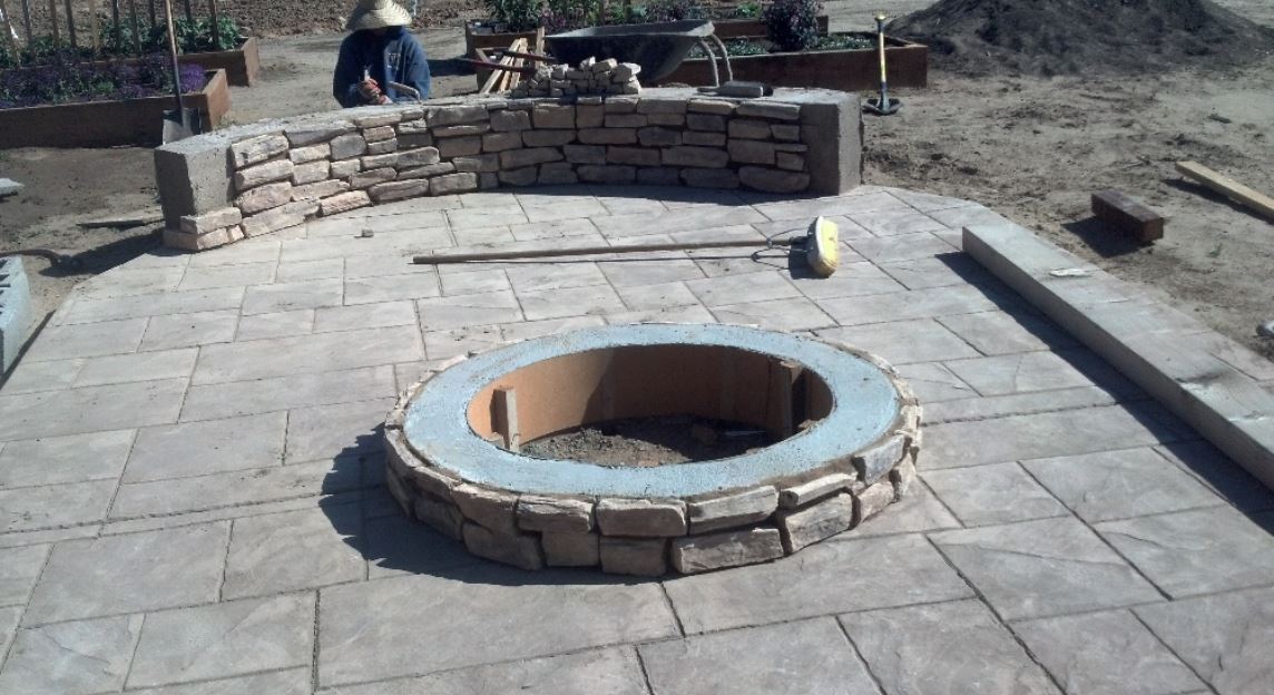 A concrete contractor working on a stacked stone fireplace set up with a stamped concrete patio